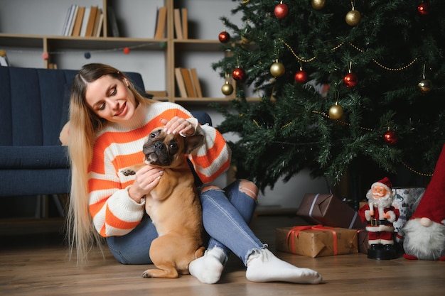 美しい女性は、飾られた部屋のクリスマス ツリーの背景に犬と一緒にヴィンテージのソファに座って新年あけましておめでとうございます