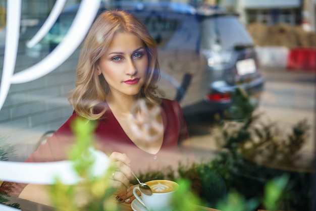 Bella donna che si siede vicino alla finestra in un caffè che beve caffè.