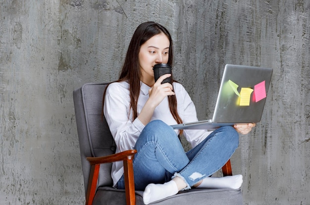 Beautiful woman sitting on chair, drinking coffee and playin on laptop. High quality photo