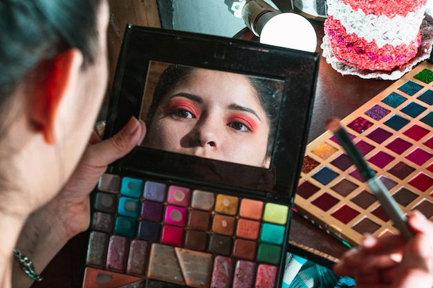 Beautiful woman sitting in front of her dressing table looking in the mirror of her eye shadow