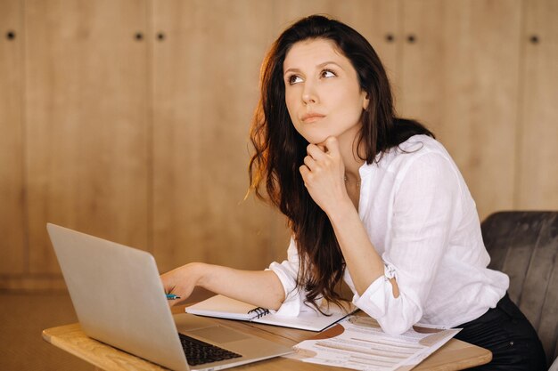 Красивая женщина сидит в офисе и работает на ноутбуке