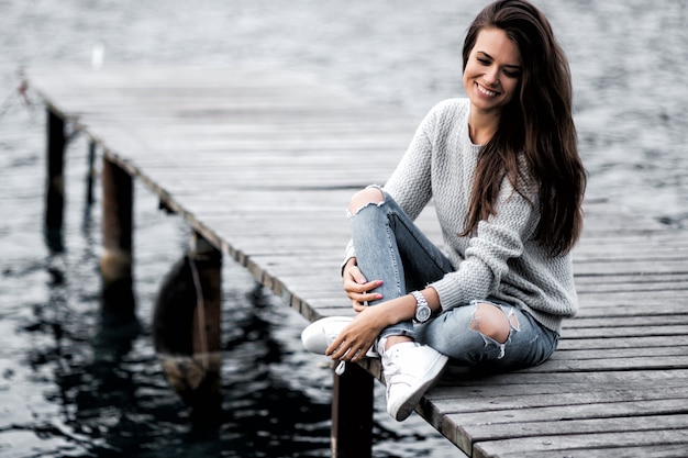 Beautiful woman sitting on the pier by the lake.