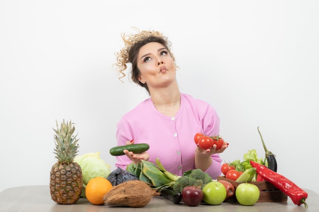 Beautiful woman sitting at table and holding red fresh tomatoes.