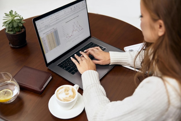 beautiful woman sitting at table studying using laptop reading a book,  surfing internet