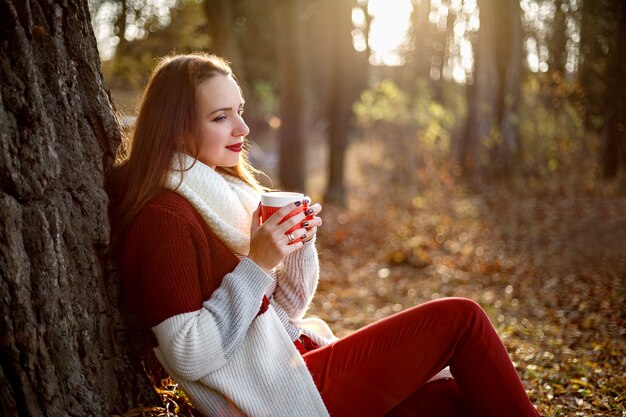 Beautiful woman sitting under a tree with a cup of mulled wine in her hands.