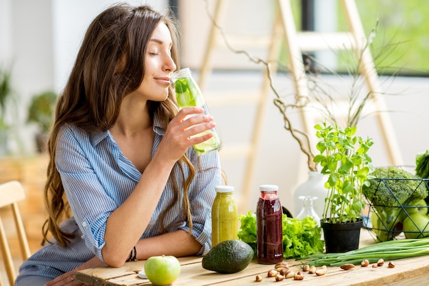 Foto bella donna seduta con bevande e cibo verde sano a casa. pasto vegano e concetto di disintossicazione