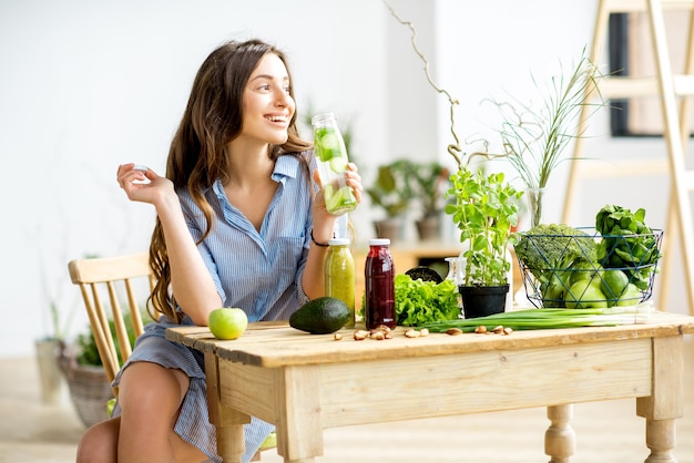 집에서 건강한 녹색 음식과 음료를 들고 앉아 있는 아름다운 여성. 채식주의 식단과 해독 개념