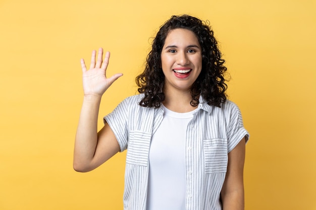 Beautiful woman smiles toothily raises palm greets friend saying hello or goodbye