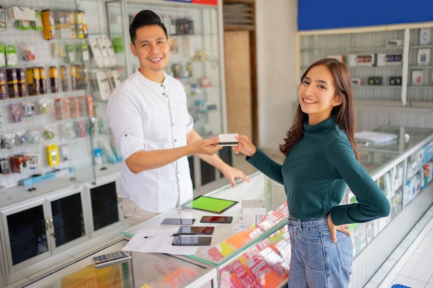 A beautiful woman smiles while giving a credit card to a man when paying