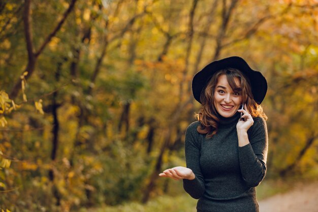 Beautiful woman smiles while talking on the phone. Cheerful girl walks in the autumn in the park