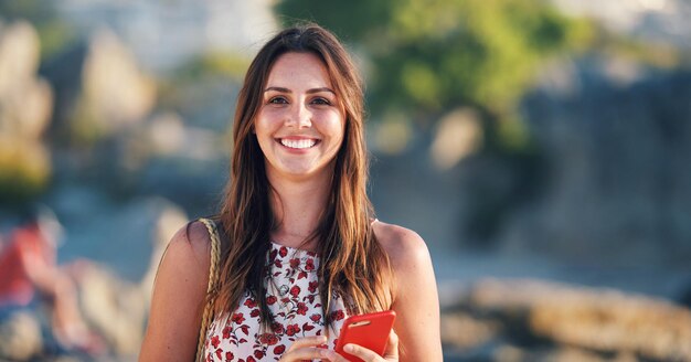 Beautiful woman smiling on beach at sunset holding smartphone enjoying travel vacation lifestyle