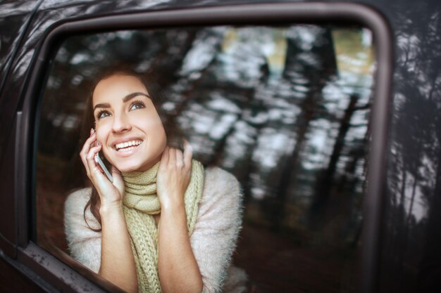 Beautiful woman smiling while sitting on the passenger seats in the car. Girl is using a smartphone