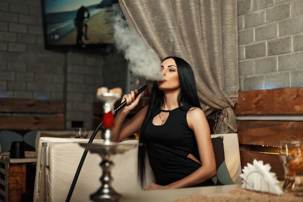 The beautiful woman smokes a hookah and lets the smoke