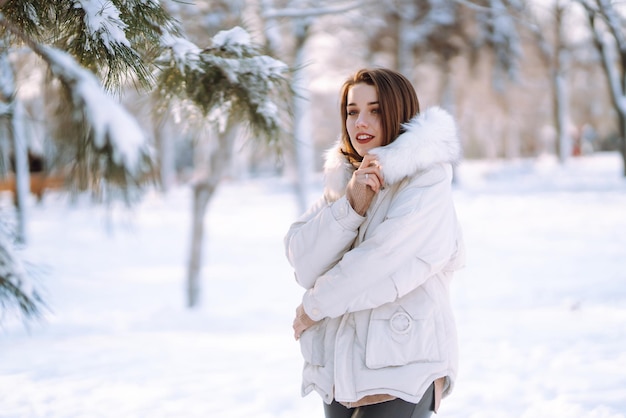 雪に覆われた公園で美しい女性。晴れた冬の日に歩く若い女性。