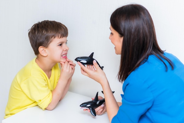 Beautiful woman speech therapist teaches boy the correct pronunciation of words and sounds in the office