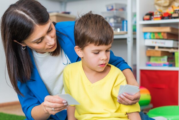 Beautiful woman speech therapist teaches boy the correct pronunciation of words and sounds in the office