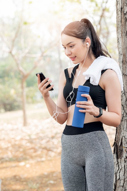 Beautiful woman in sportswear holding water bottle and using smartphone after running.