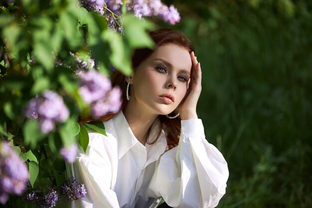 Beautiful woman in spring in the branches of flowering lilac bushes