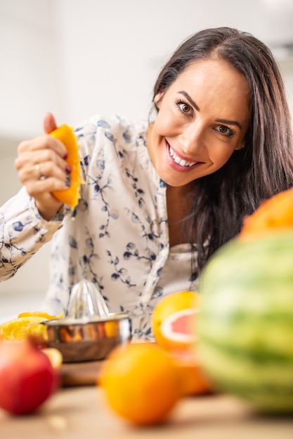 Beautiful woman squeezes orange with fruits on the table.