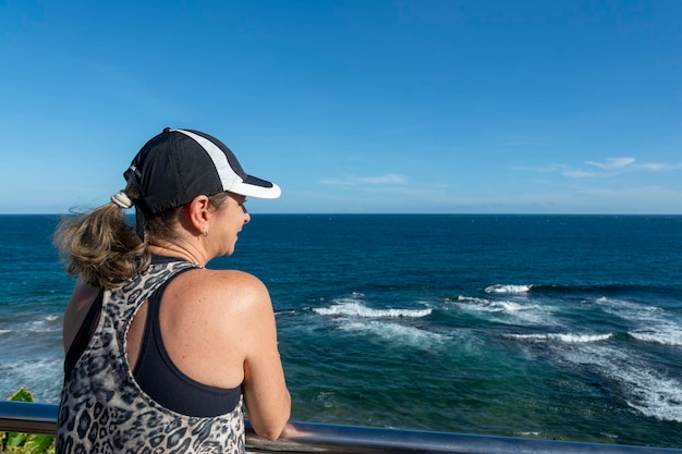 Photo beautiful woman standing enjoying the beautiful sea beautiful day with strong sun and blue sea back view