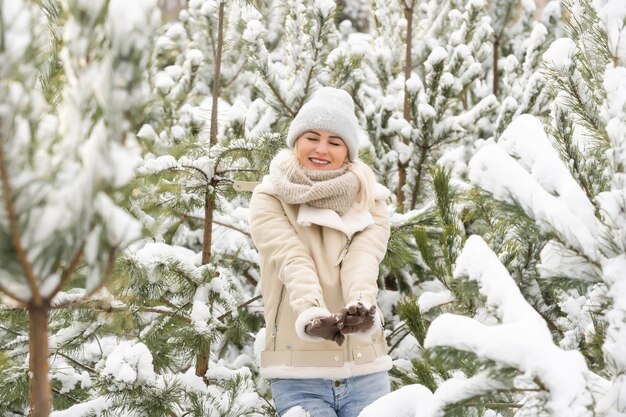 Beautiful woman standing among snowy trees in winter forest and enjoying first snow. Woman in winter woods. pines