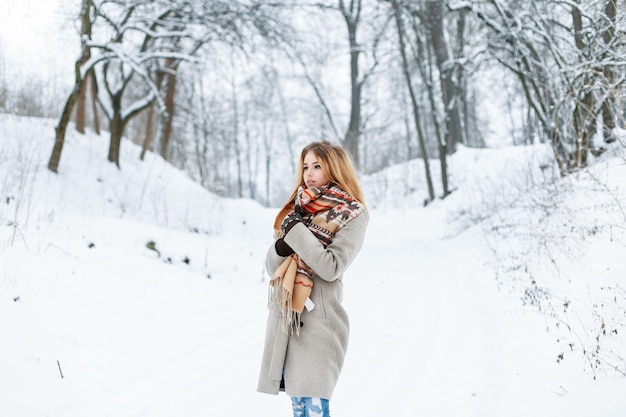 Beautiful woman standing in a winter park near a tree in a stylish vintage clothing