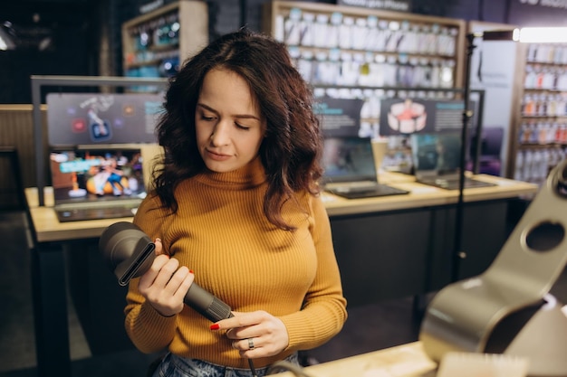 Beautiful woman in the store is testing a hairdryer