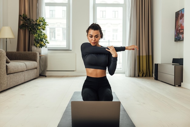 Foto bella donna che si allunga a casa mentre guarda il portatile