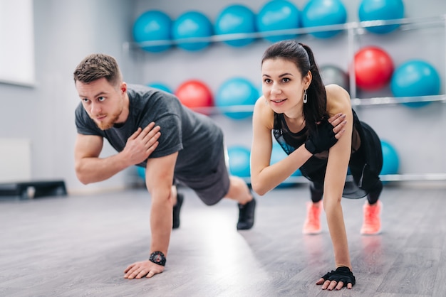 Beautiful woman and strong male doing push-ups on one hand