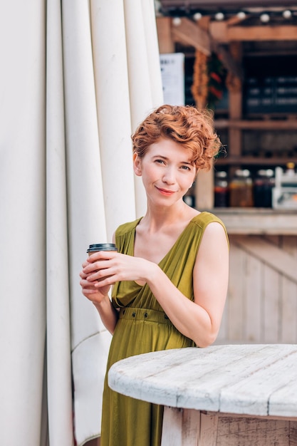 A beautiful woman in a summer cafe with coffee in her hands looks at the camera with a smile