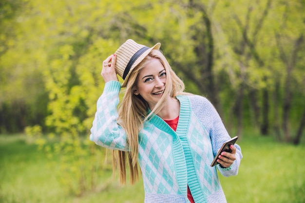 Beautiful woman in summer Park happy and smiling with mobile phone in hand and hat on head