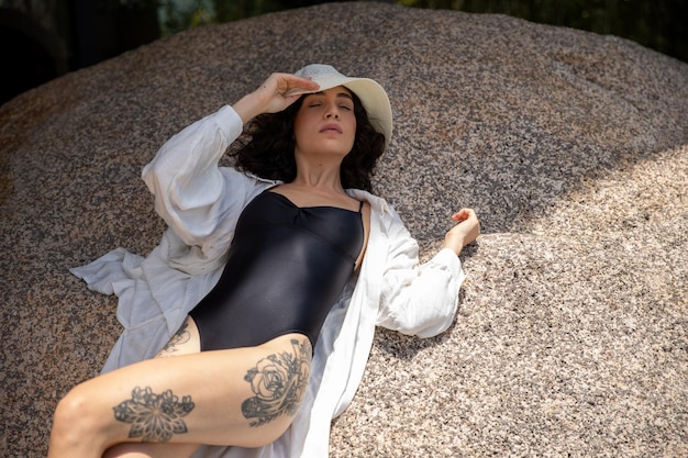 beautiful woman sunbathing, woman wearing hat leaning on a rock outdoors, summer vacation