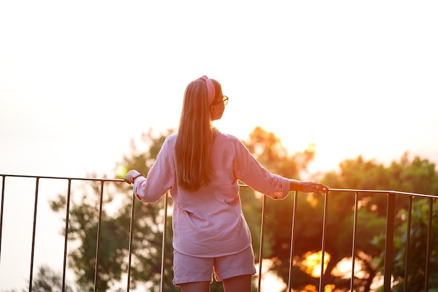 석양의 아름다운 여인은 바다가 내려다 보이는 테라스에 선다. 고품질 사진