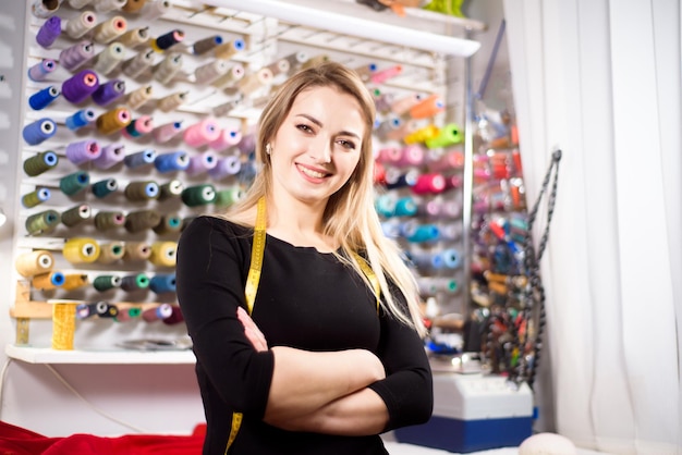 Beautiful woman tailor on background of colored spools of thread for sewing and embroidery