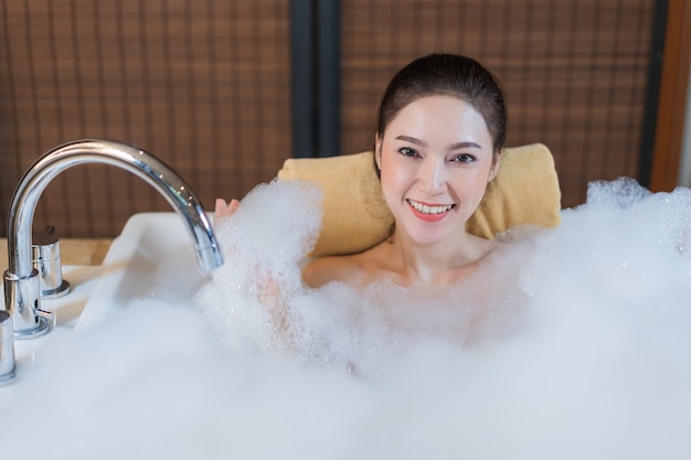 美しい女性がバブルバスを浴びて浴槽で遊ぶ
