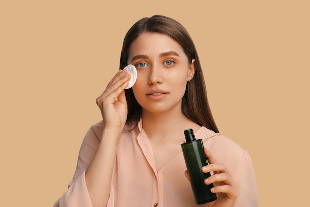 Beautiful woman takes off her make up while holding cotton disk and cleanser