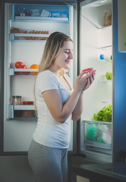 Beautiful woman taking donut from fridge at late evening