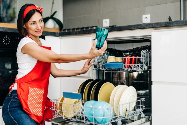 Beautiful woman taking out clean dishes from dishwasher machine.
