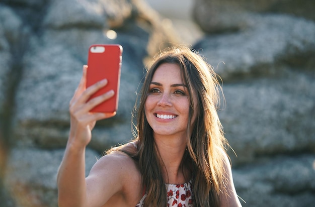 夕暮れ時のビーチでスマートフォンを使用して写真を撮る美しい女性