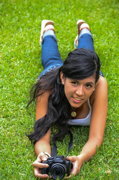 Beautiful woman taking photos with a digital camera, lying on the greenery.