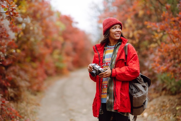 秋の森で写真を撮る美しい女性 秋の天気を楽しむ笑顔の女性