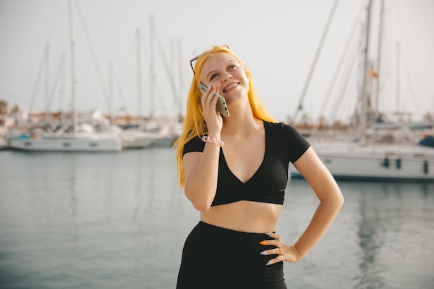 Bella donna che parla al telefono sullo sfondo del mare blu e degli yacht