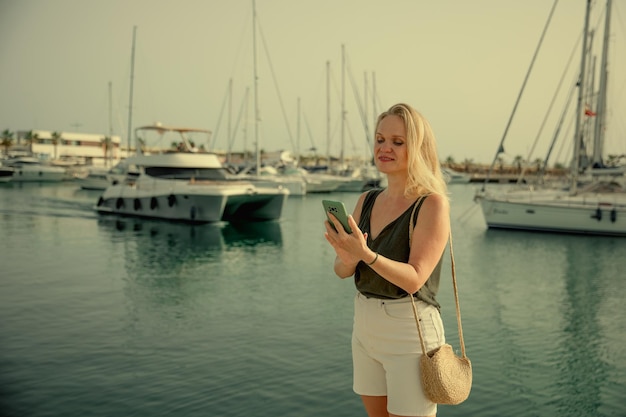 Bella donna che parla al telefono sullo sfondo del mare blu e degli yacht