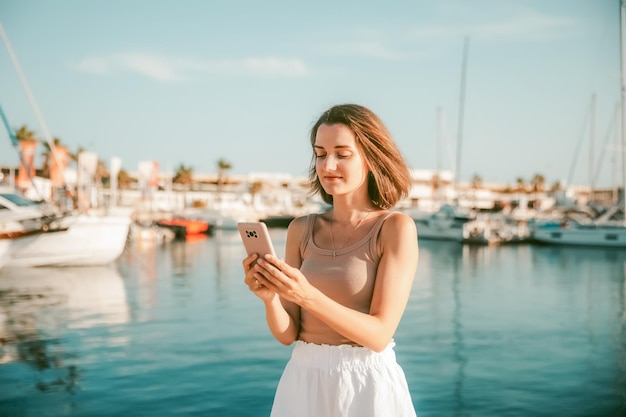 Bella donna che parla al telefono sullo sfondo del mare blu e degli yacht