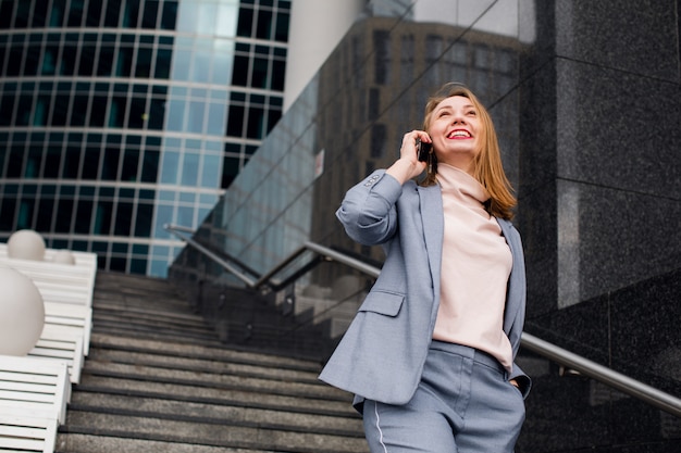 Beautiful Woman Talking On Phone Walking On Street. Portrait Of Stylish Smiling Business Woman In Fashionable Clothes Calling On Mobile Phone Near Office