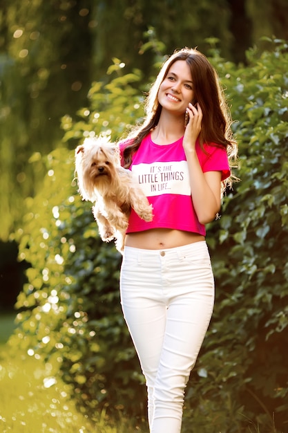 Photo beautiful woman talking on the phone while walking with a dog in the park