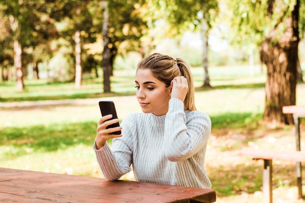 緑の背景の公園でスマートフォンで美しい女性のテキストメッセージ。