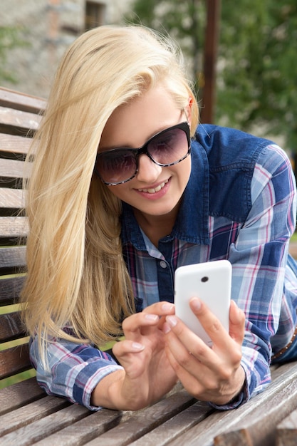 Beautiful woman texting with her phone on bench in park