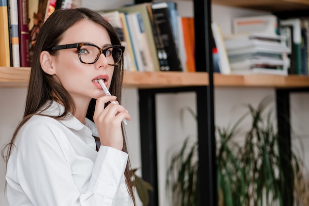 Beautiful woman thinks with pen in her mouth