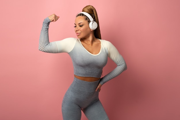 beautiful woman in a tracksuit on a pink background with headphones